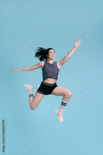 Portrait beautiful smiling woman wearing sportswear jumping high looking away, isolated on blue background. Successful professional runner, athlete training, doing exercises . Sport, healthy lifestyle