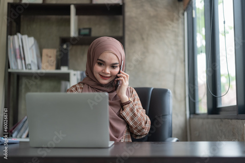 Beautiful muslim businesswoman or female executive manager wearing hijab sits at her worktable and uses a smartphone.