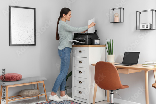 Woman using modern printer on chest of drawers at home photo