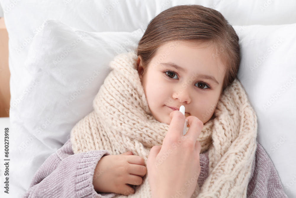 Mother using nasal spray to treat her little daughter on bed, above view Mother using nasal spray to treat her little daughter on bed, above view