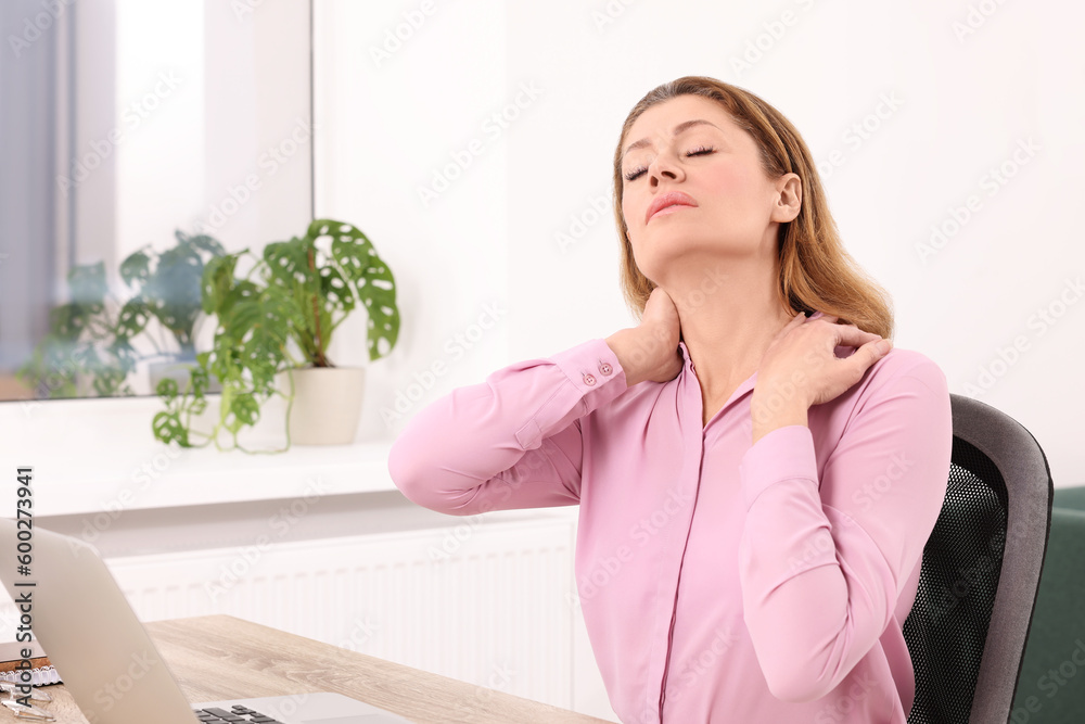 Woman suffering from pain in shoulders at wooden table indoors. Arthritis symptoms Woman suffering from pain in shoulders at wooden table indoors. Arthritis symptoms