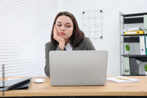 Puzzled young intern using laptop at table in modern office. First work day