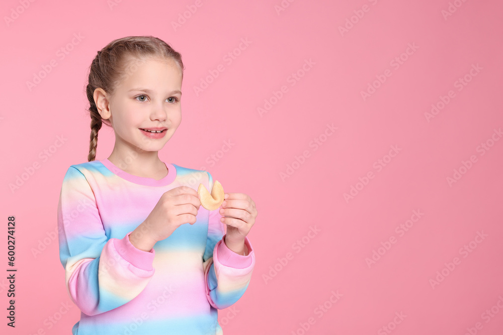 Cute girl holding tasty fortune cookie with prediction on pink background. Space for text Cute girl holding tasty fortune cookie with prediction on pink background. Space for text