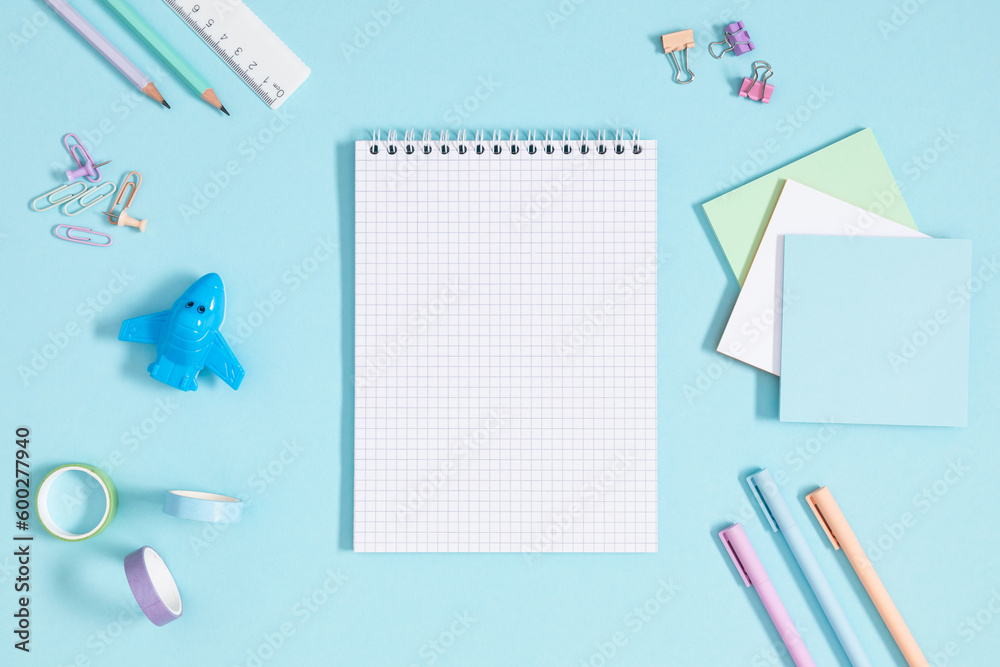 Back to school concept. Flat lay top view of scattered stationery notepad pens pencils paper clips airplane sticky tape note paper isolated on pastel blue background Back to school concept. Flat lay top view of scattered stationery notepad pens pencils paper clips airplane sticky tape note paper isolated on pastel blue background
