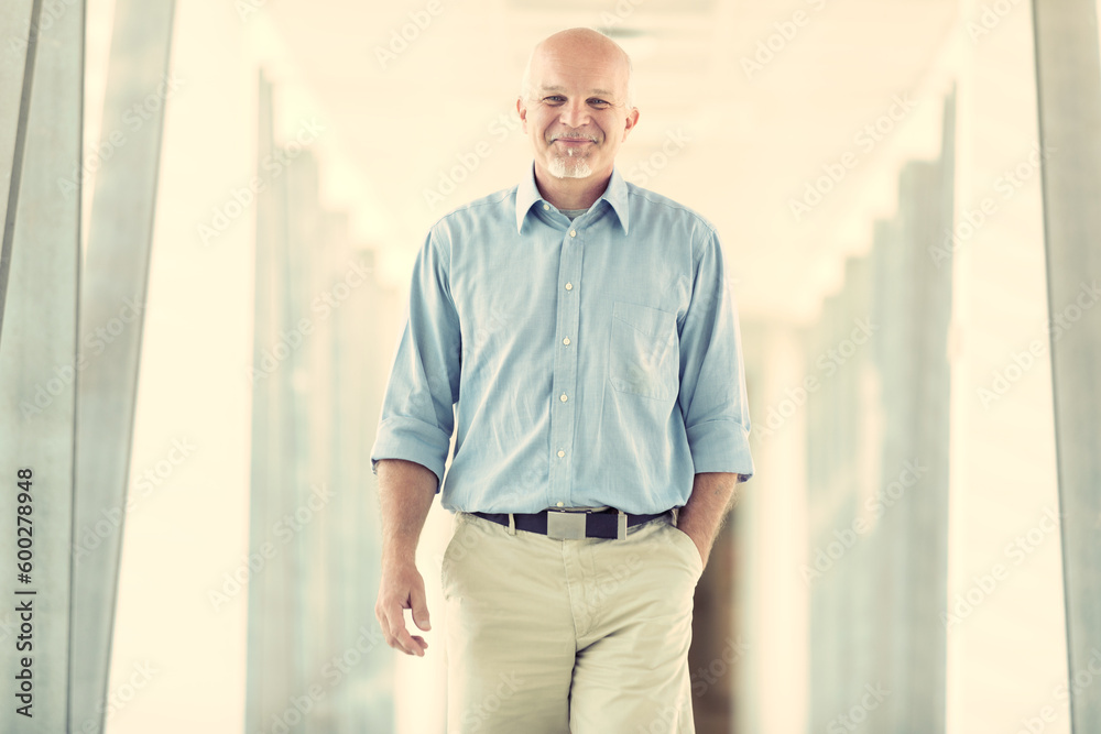 Smiling man approaches walking down a bright corridor of a moder Smiling man approaches walking down a bright corridor of a moder