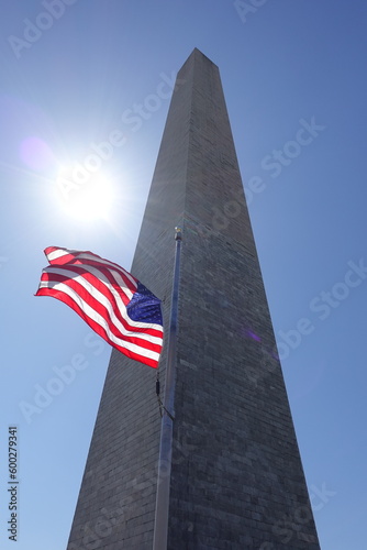 Washington monument with an American flag during noon with the sun near it creating sunstars