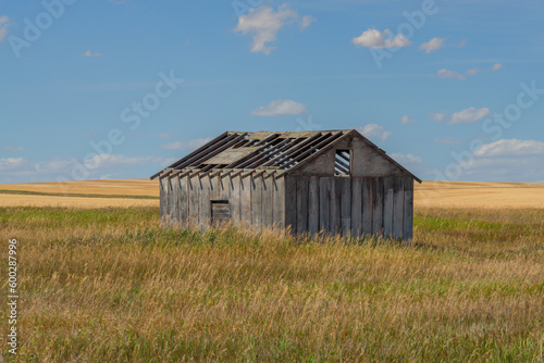 Old abandoned farm building in the prairie with a cloudy blue sky
