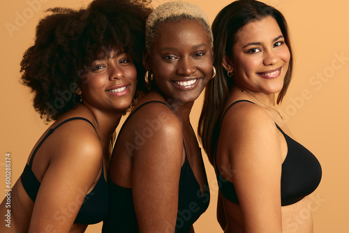 Delighted young multiracial female models smiling in beige studio