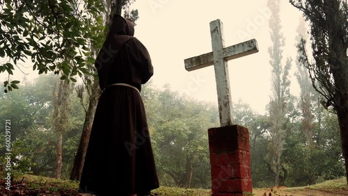 Fraile Franciscano monje meditando y contemplando la cruz sobre terreno campo en montaña en un día nublado al amanecer al aire libre en el bosque