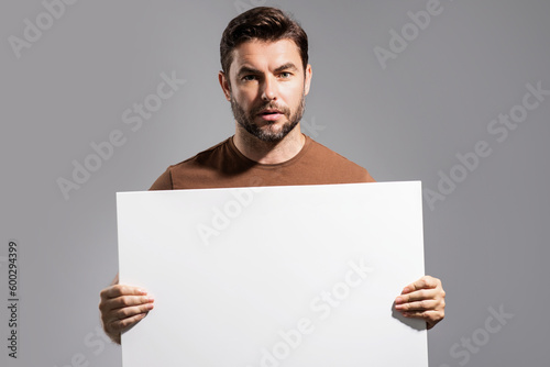 Man with empty blank banner ad on studio background. Portrait of attractive man holding empty blank poster. Man showing blank poster. Male presenting signboard, board or banner with copy space.