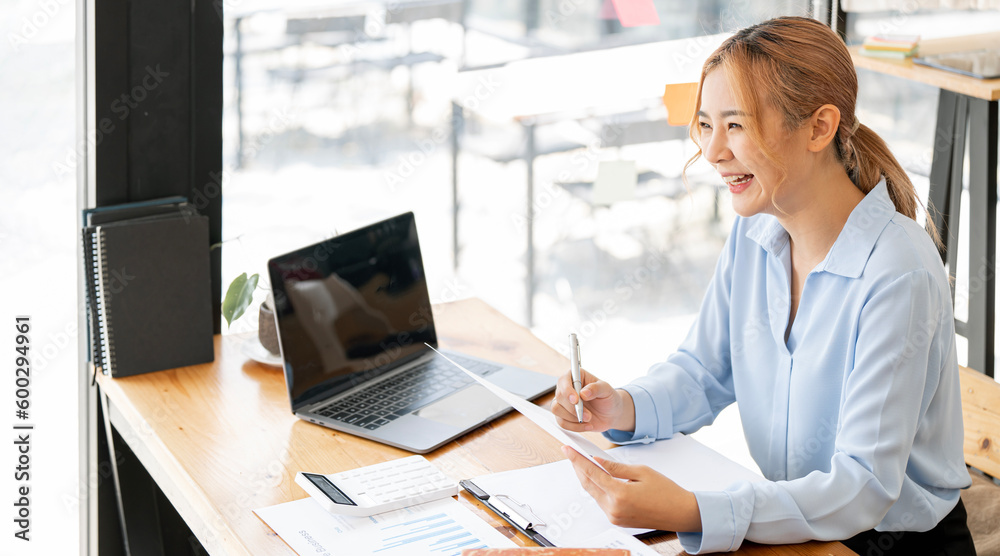 Image of smiling beautiful woman writing down notes while sitting at table in office Image of smiling beautiful woman writing down notes while sitting at table in office
