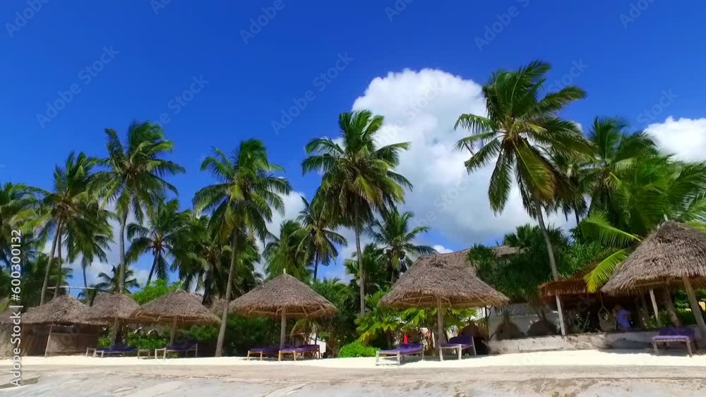 straw parasol and deckchair on a white sand beach with coconut trees in the background