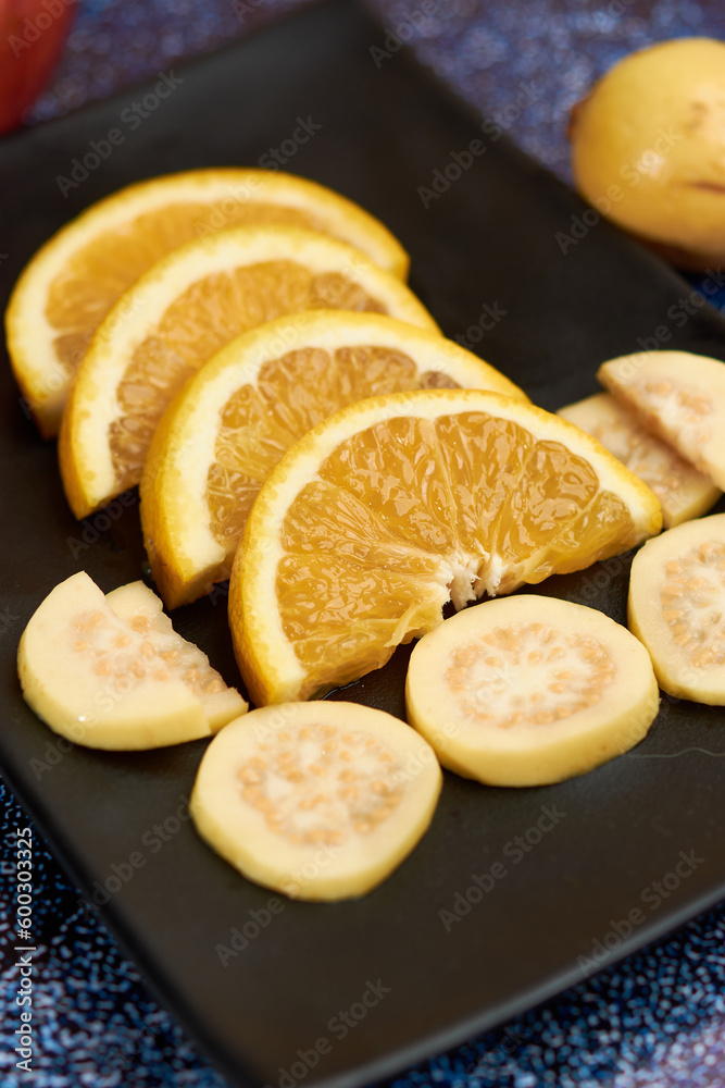 Plate of orange cut into segments, with guavas around it black Plate,