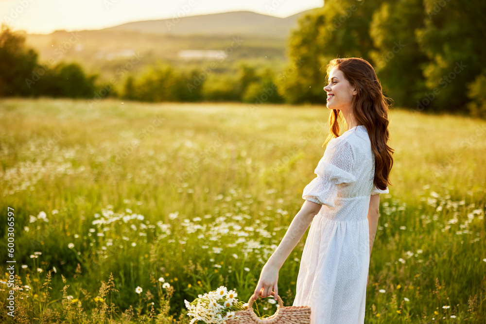 happy woman in a light dress and a wicker basket full of daisies enjoys nature walking in the field happy woman in a light dress and a wicker basket full of daisies enjoys nature walking in the field