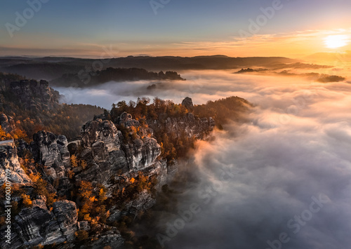 Saxon, Germany - Aerial panoramic view of the Bastei on a foggy autumn morning with colorful autumn foliage and heavy fog under the rock. Bastei is a rock formation in Saxon Switzerland National Park