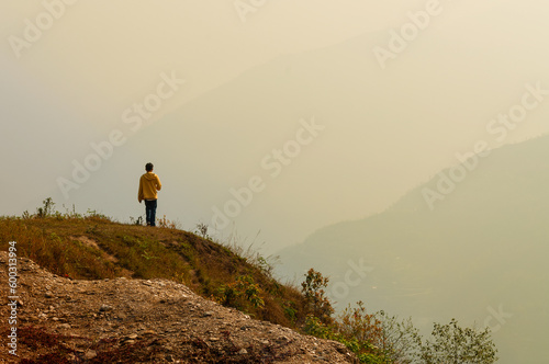 A single man standing at the edge of the cliff and looking at distant Himalayan mountians. Trekking route towards Varsey Rhododendron Sanctuary or Barsey Rhododendron Sanctuary. Sikkim, India. photo