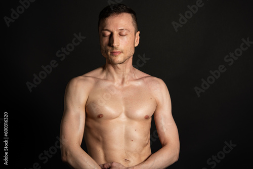 Young attractive man with an athletic body on a black background. © vladorlov