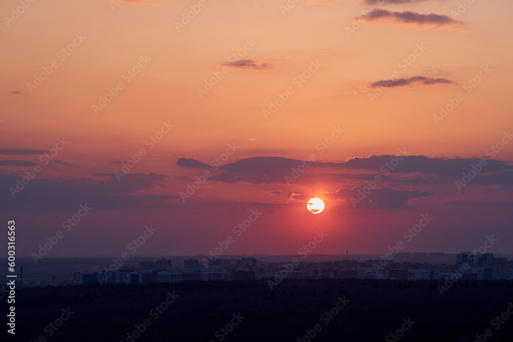 Red sun in the sunrise sky in the light of rays from behind the clouds