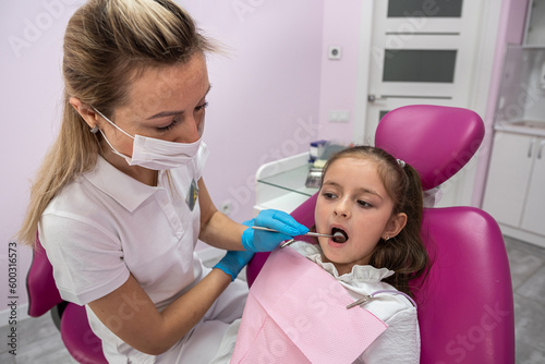 beautiful little female patient grimaces during oral examination by female dentist.