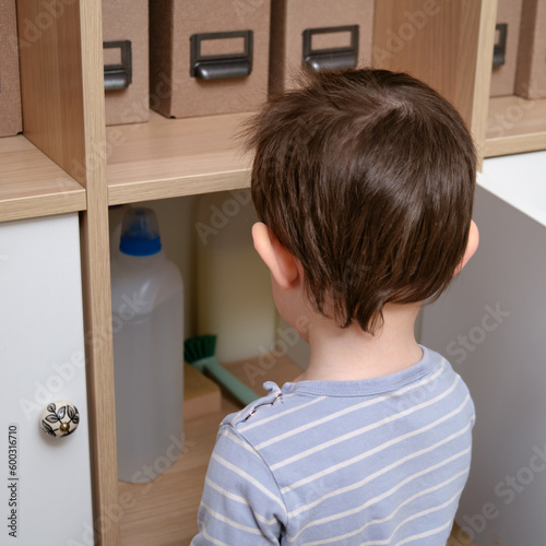 Toddler baby plays with household chemicals and detergent from the closet. Child boy with detergent bottle in home living room. Kid age one year nine months