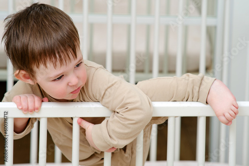 Baby escapes from the crib by climbing over the bars. The child climbs over the railing bed. Kid aged about two years (one year nine months)