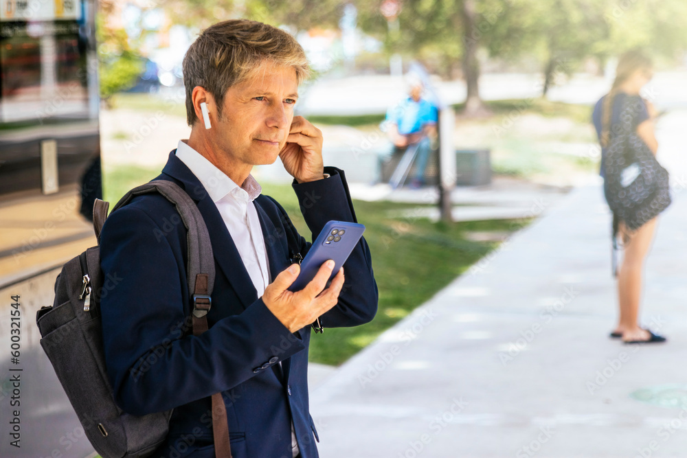 Businessman waiting for the train uses wireless headphones to have a phone conversation