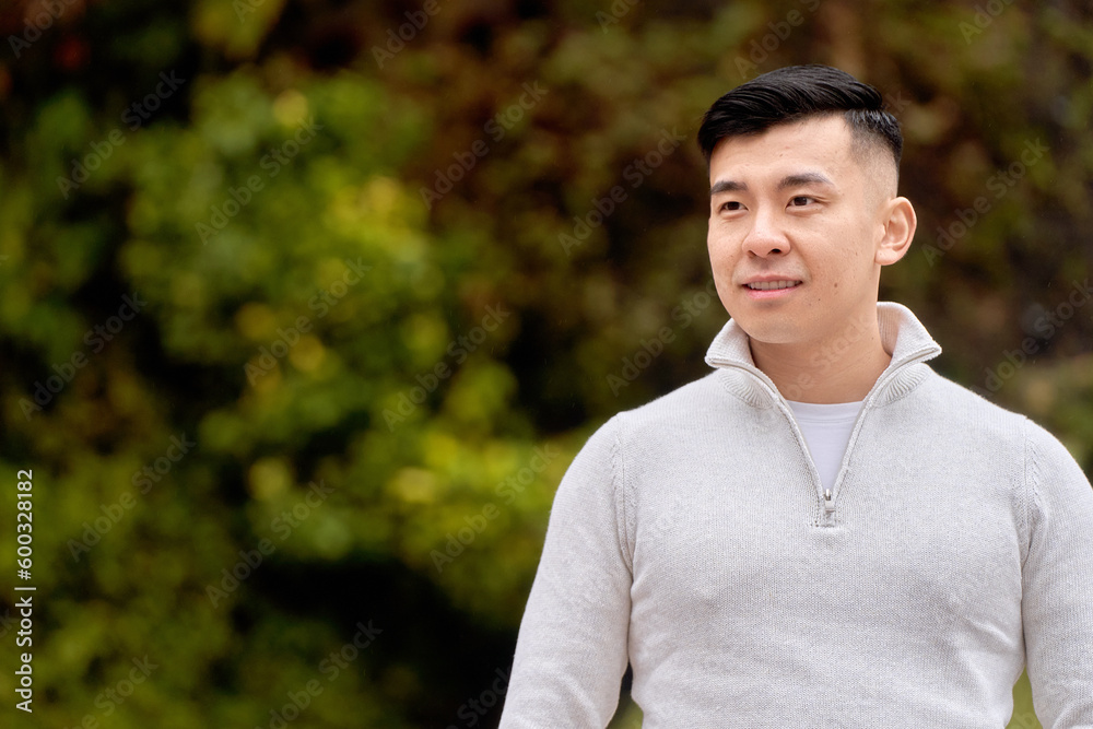 Attractive Asian man looking to the side smiling while relaxing outdoors in a park. Attractive Asian man looking to the side smiling while relaxing outdoors in a park.