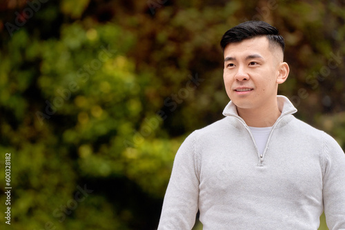 Attractive Asian man looking to the side smiling while relaxing outdoors in a park. 
