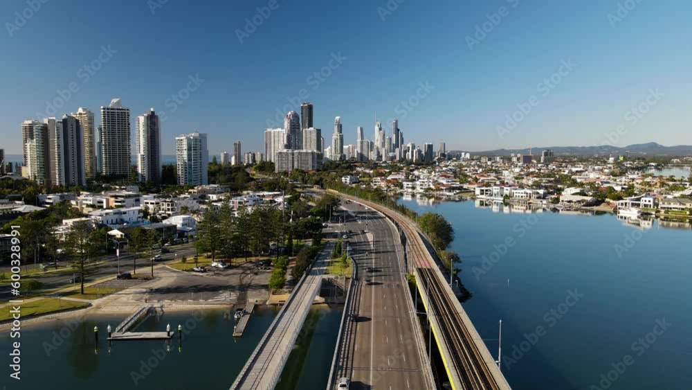 Cars travel along a modern multi lane urban bridge leading into an inner city towering high-rise skyline. Drone view