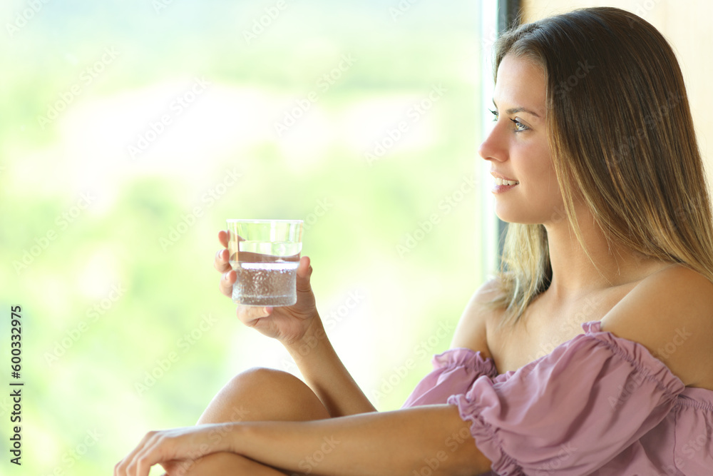 Happy teen holding glass of water looks through a window