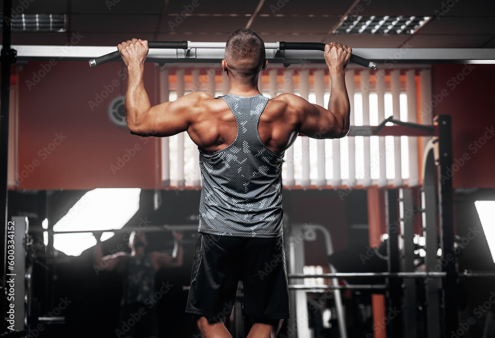 Naklejka premium Man doing pull-up exercises on horizontal bar in gym, Back view