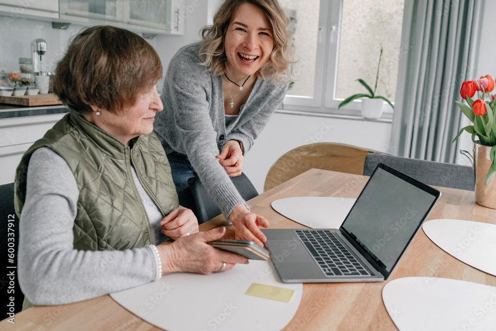 Happy granddaughter by senior woman with laptop on table at home Happy granddaughter by senior woman with laptop on table at home