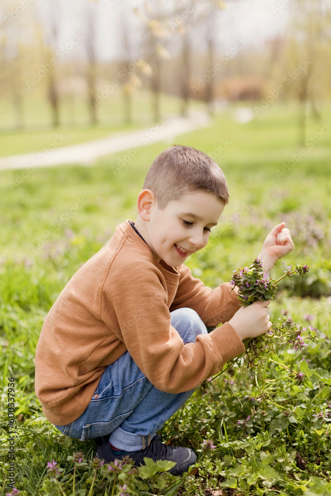 Smiling boy holding flowers crouching in park Smiling boy holding flowers crouching in park