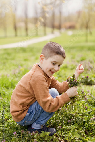 Smiling boy holding flowers crouching in park photo