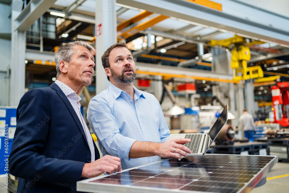 Manager and businessman looking up by solar panel at factory Manager and businessman looking up by solar panel at factory