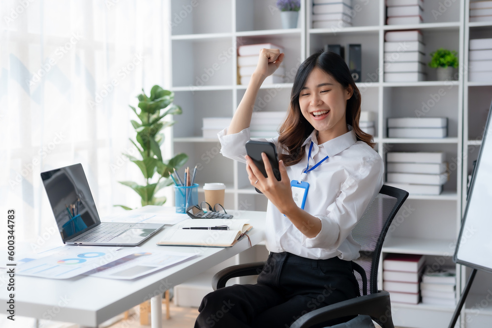 Happy asian businesswoman raising hands with victory smiling happily with smart phone. The concept of success at work.