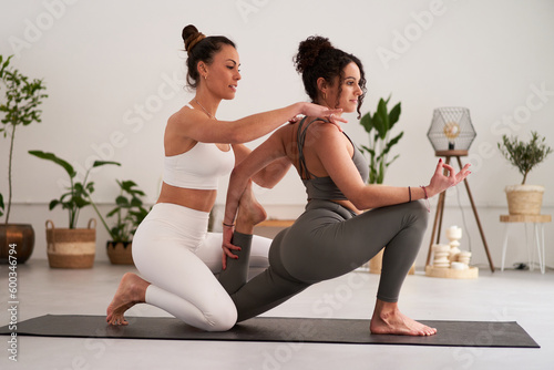 Female yoga instructor helping her student to master a position during private class in the studio. Mental health activity. Two young women doing sport exercises. photo