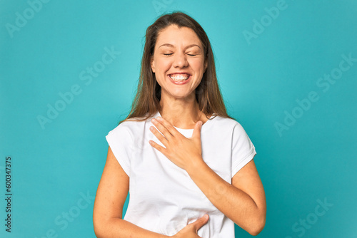 A young caucasian woman isolated laughs happily and has fun keeping hands on stomach.