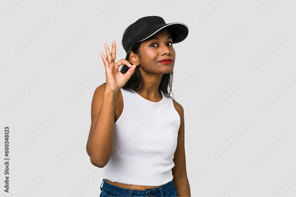 Young Indian woman cut out isolated on white background winks an eye and holds an okay gesture with hand. Young Indian woman cut out isolated on white background winks an eye and holds an okay gesture with hand.