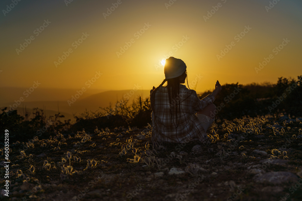 Woman tourist on top of sunrise mountain. The girl salutes the sun, wearing a jacket, white hat and white jeans. Conceptual design.