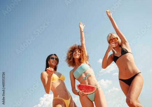 Three beautiful young woman with fruit, in swimming suites, happy, smiling outdoors in the summer.