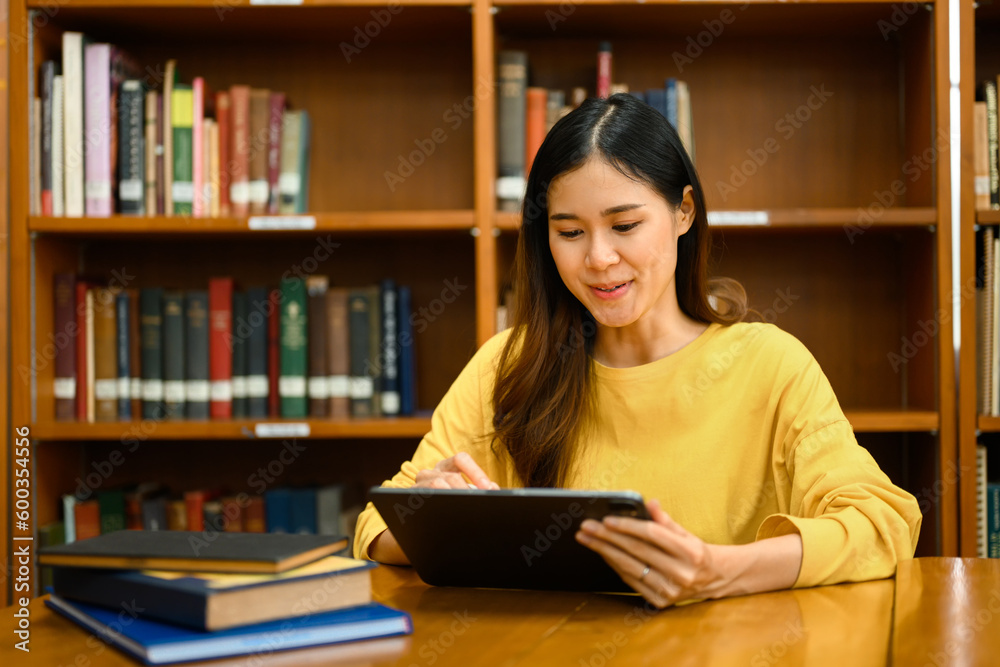 Focused asian female students using digital tablet for searching online Information in library. Education and technology concept Focused asian female students using digital tablet for searching online Information in library. Education and technology concept