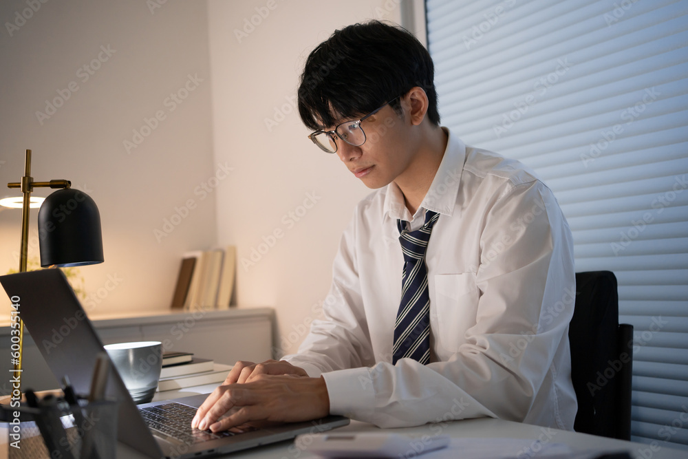 Alone Working Late at Night.Asian business man at workplace in office holding his head on hands after late night work at a desk in a dark office working on a laptop late in the evening concept Alone Working Late at Night.Asian business man at workplace in office holding his head on hands after late night work at a desk in a dark office working on a laptop late in the evening concept