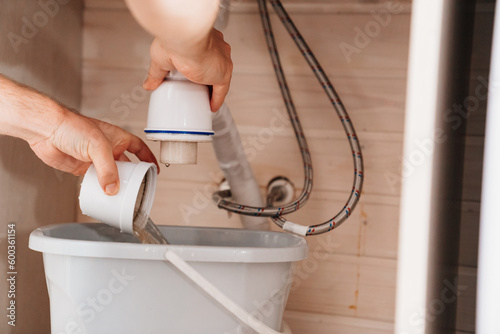 The plumber disassembles the siphon under the sink to clear the blockage. photo