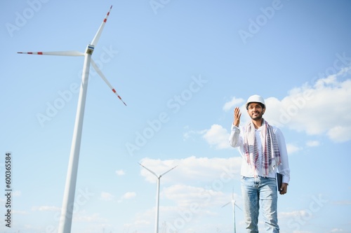 Engineer India man working at windmill farm Generating electricity clean energy. Wind turbine farm generator by alternative green energy. Asian engineer checking control electric power