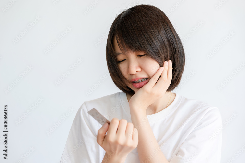 Woman holding her cheek while holding a pack of painkillers due to toothache. Woman holding her cheek while holding a pack of painkillers due to toothache.
