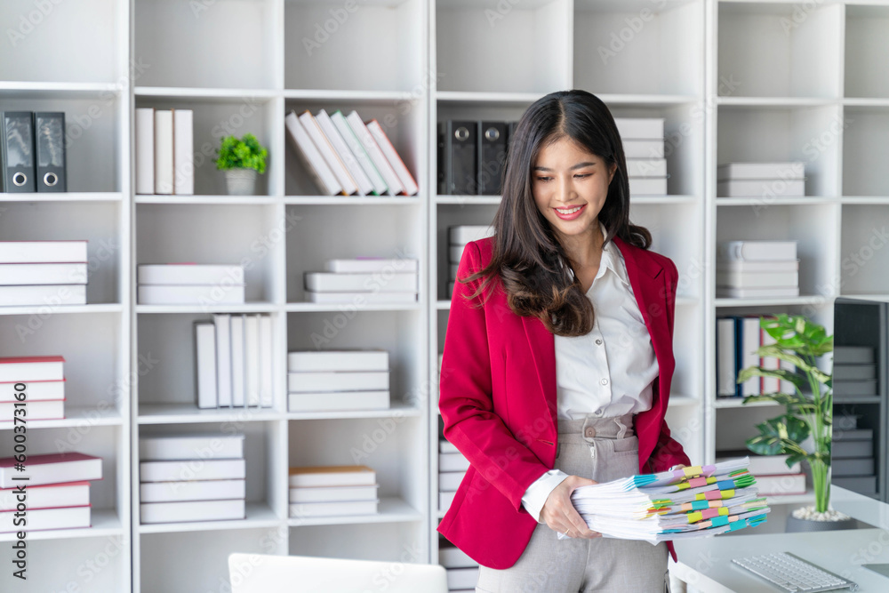 Asian happy beautiful businesswoman hold paper documents work stand at workplace. Attractive female employee office worker smile. Asian happy beautiful businesswoman hold paper documents work stand at workplace. Attractive female employee office worker smile.