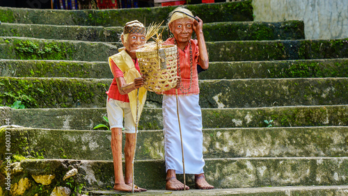 Carved statues of men and women holding bamboo bags placed on the stairs at the Londa tourist spot in Toraja photo