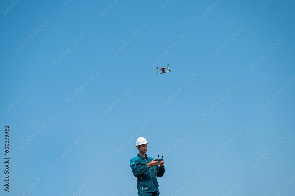 A man in a helmet and overalls controls a drone at a construction site. The builder carries out technical oversight. A man in a helmet and overalls controls a drone at a construction site. The builder carries out technical oversight.
