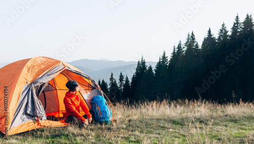 young female hiker with backpack near the tent in the mountains enjoying the leisure and freedom